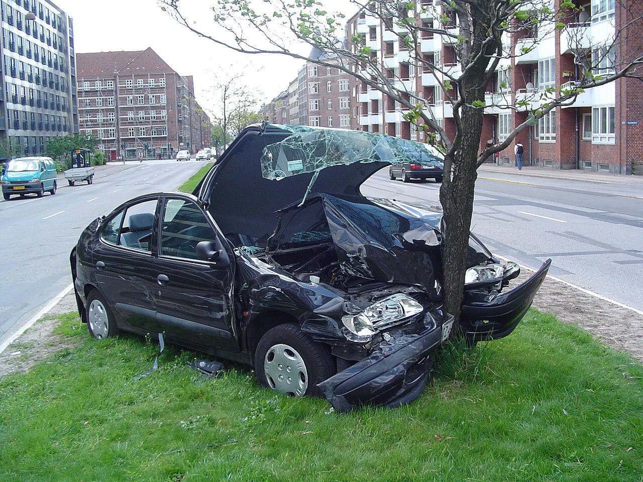 Een zwarte auto is op een boom in gereden. De auto is zwaar beschadigd.