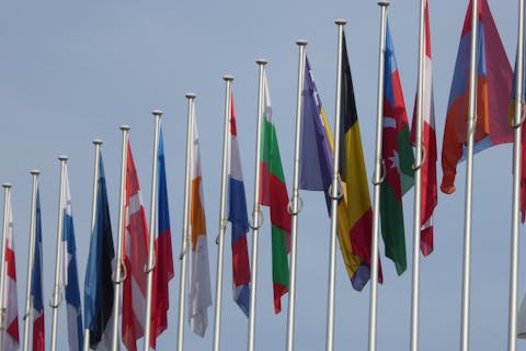 Veel lidstaten van de EU houden vast aan hun eigen regels en gebruiken. Een rij vlaggenmasten met verschillende vlaggen die naar beneden hangen. De lucht is lichtblauw.