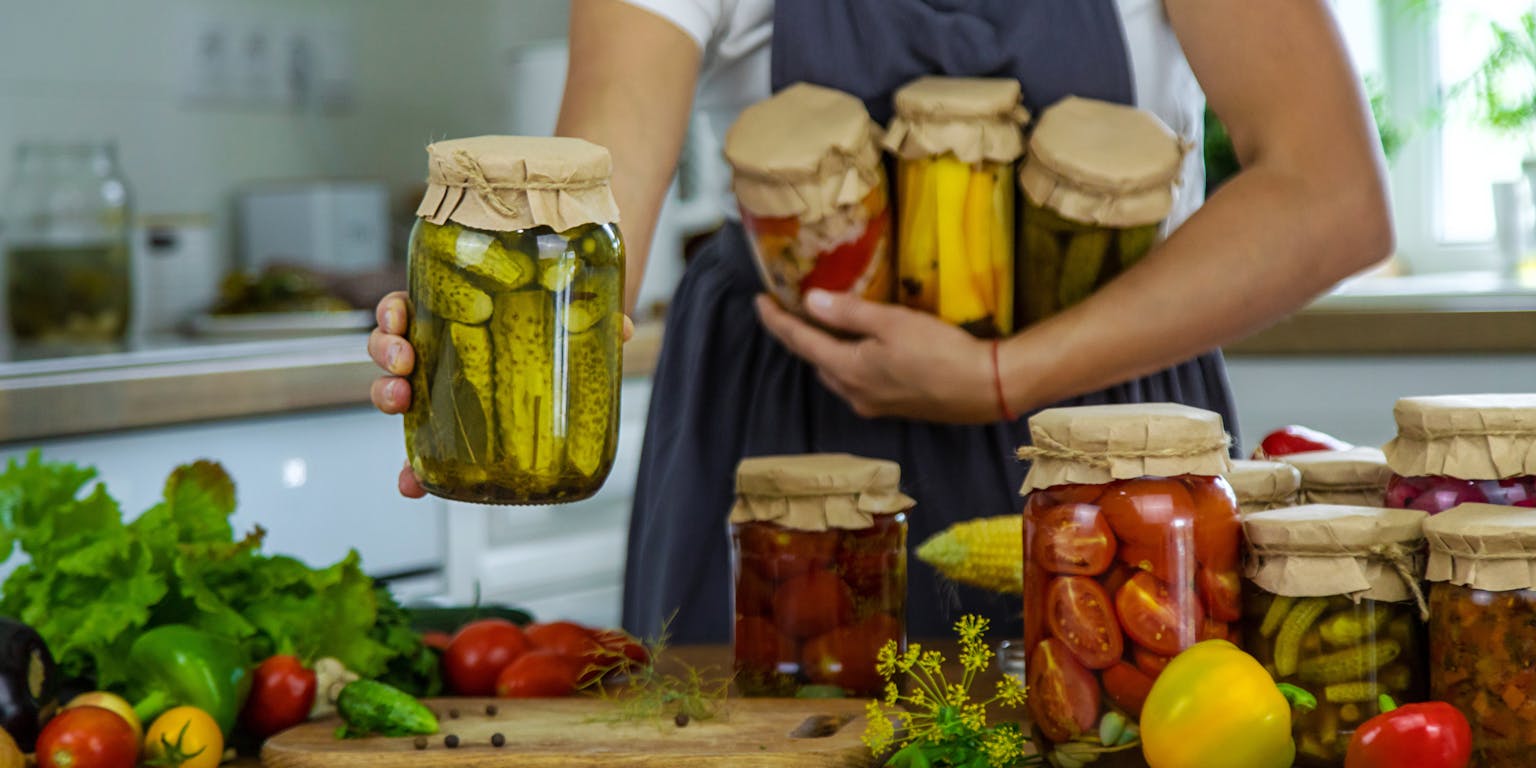 gefermenteerde, ingemaakte groenten in verschillende glazen potten en jonge vrouw die ze vasthoudt