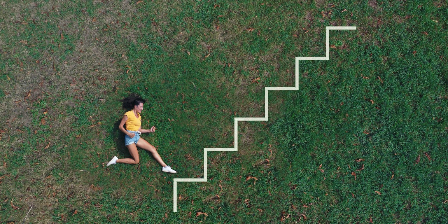 Jonge vrouw ligt in het groene gras en lijkt zo een ladder te beklimmen