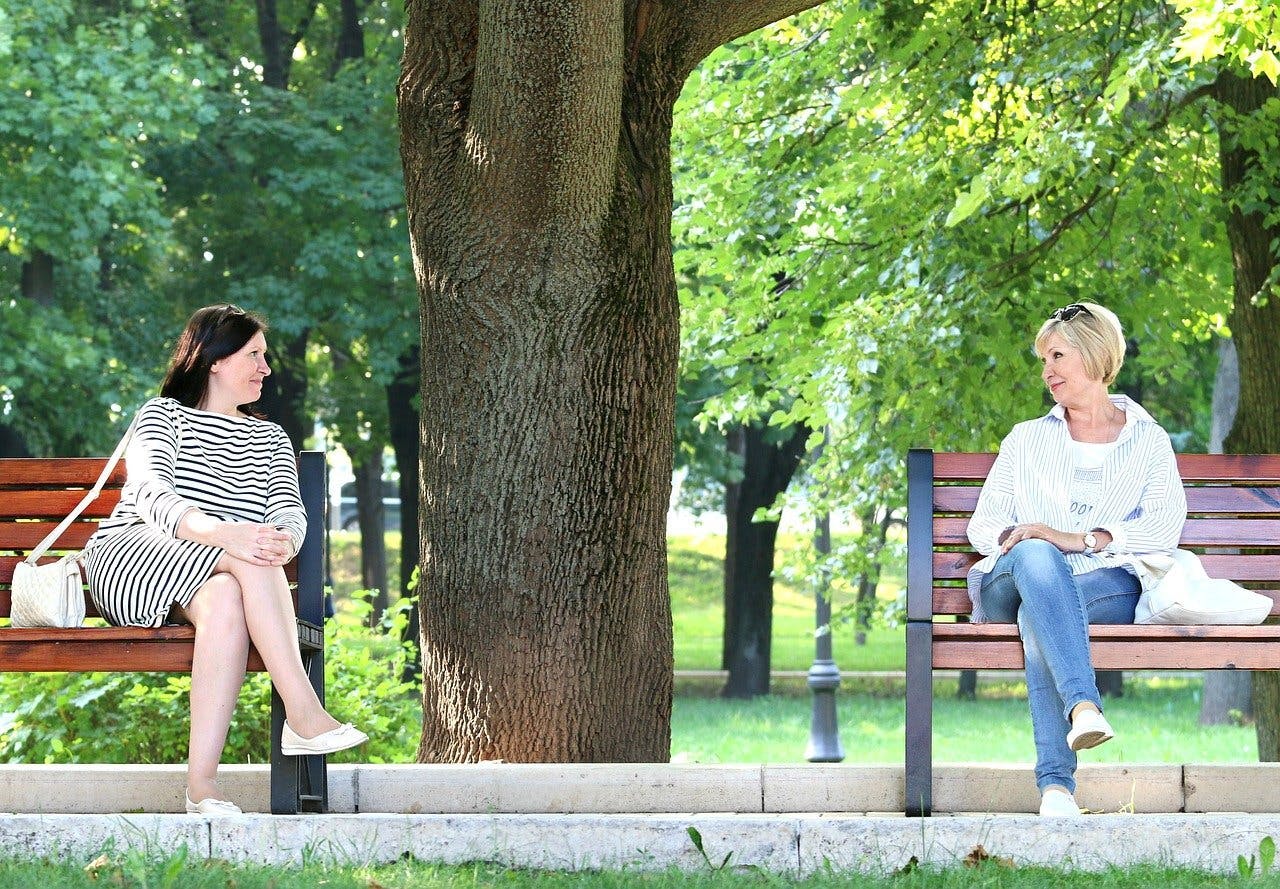 Twee vrouwen zitten op een eigen bankje in een park.