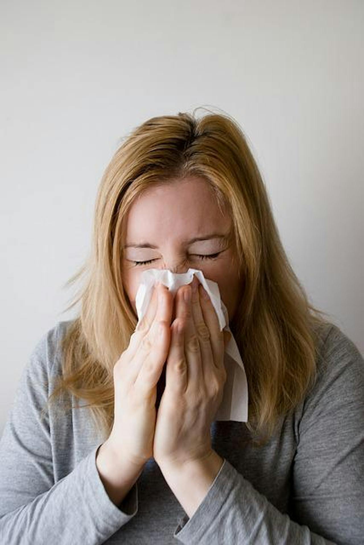 Een vrouw snuit haar neus met een tissue.
