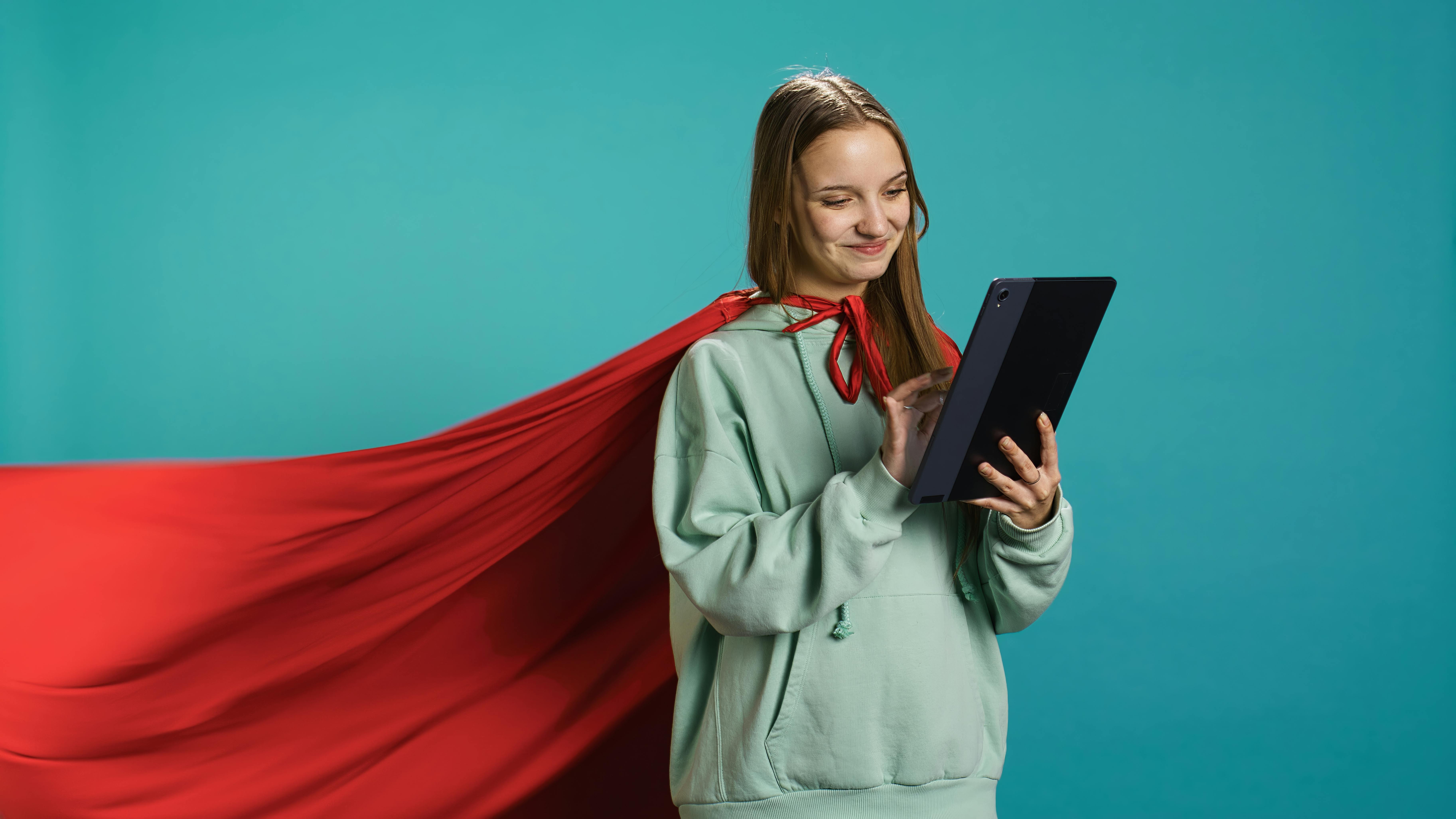 Een jonge vrouw met een laptop draagt een rode supermancape