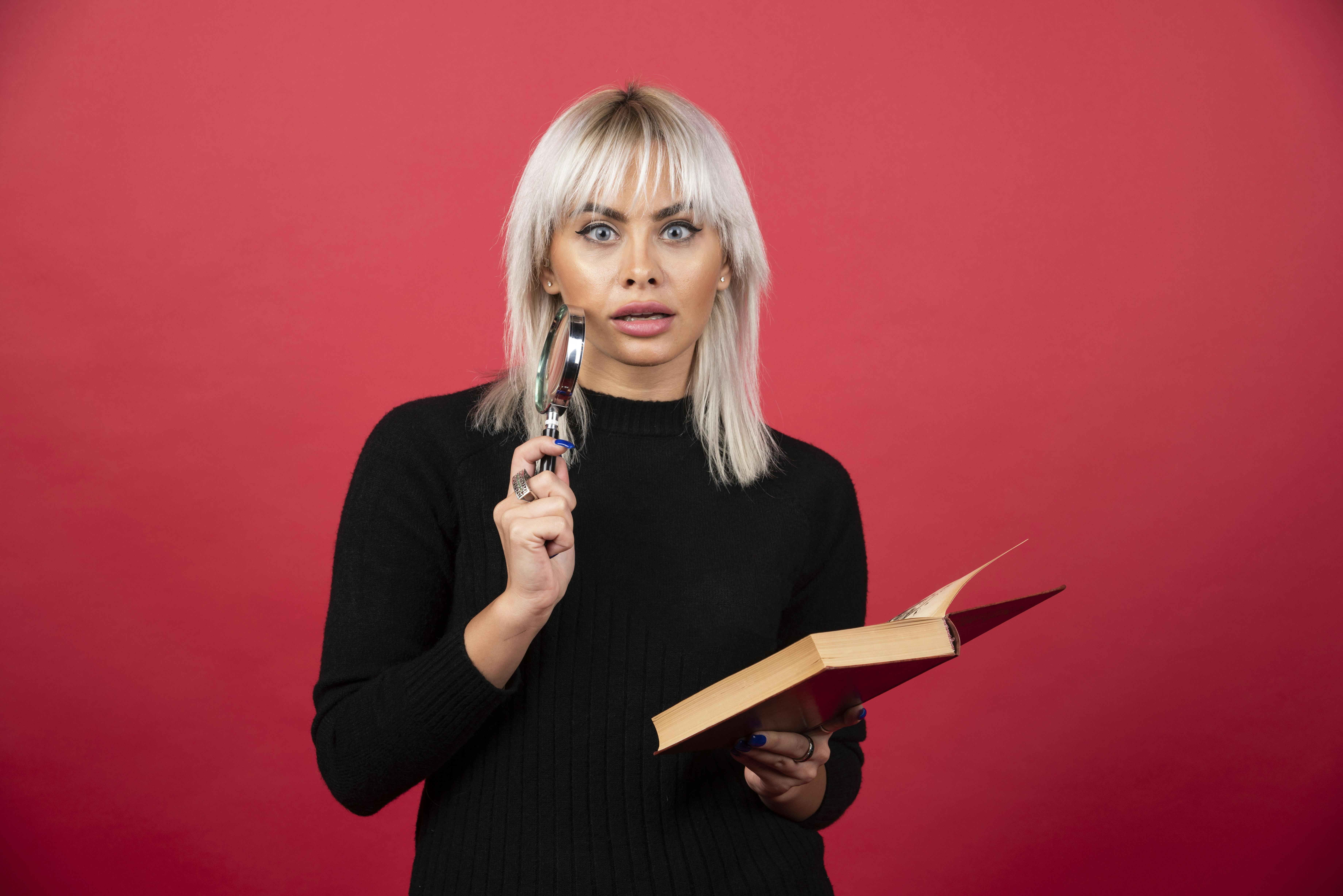 Jonge vrouw kijkt geschokt terwijl ze een boek en een loep vasthoudt