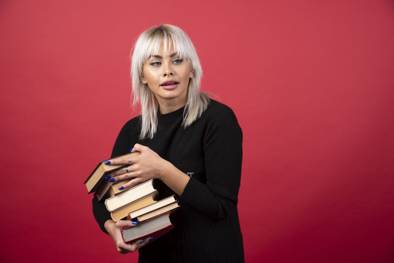 Jonge geblondeerde vrouw houdt een stapel boeken vast