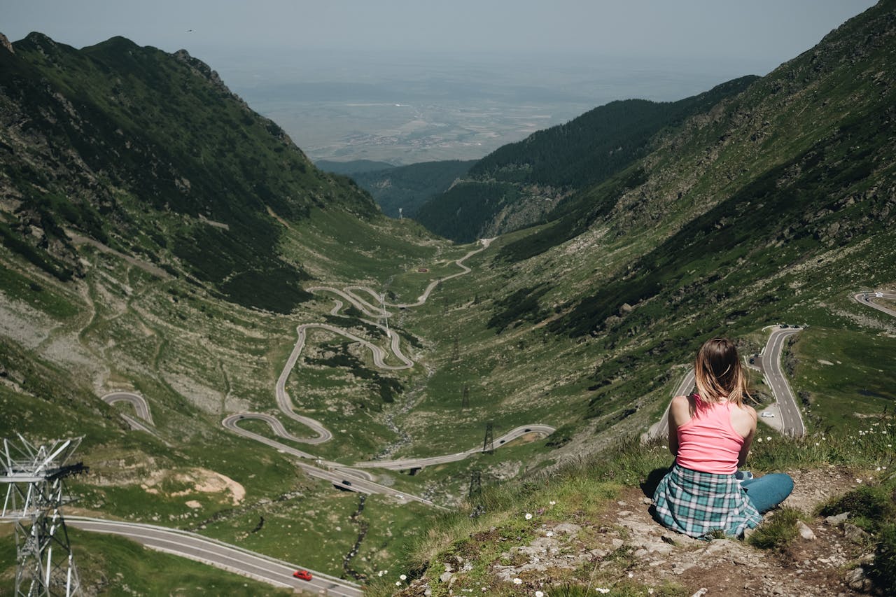 jonge vrouw kijkt uit op berglandschap met kronkelende wegen naar de top