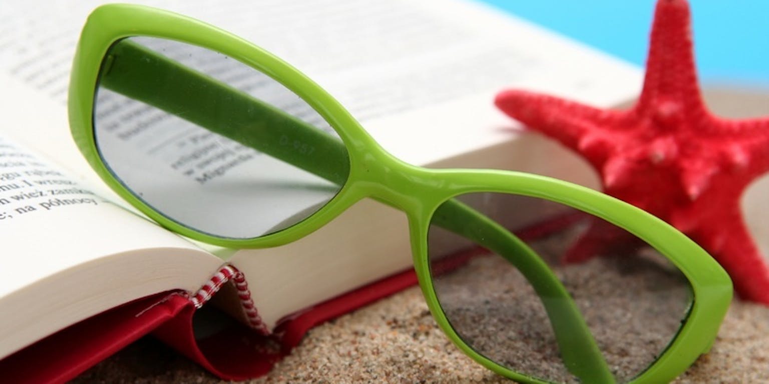 Een groene bril, een open boek en een rode zeester op het zand.