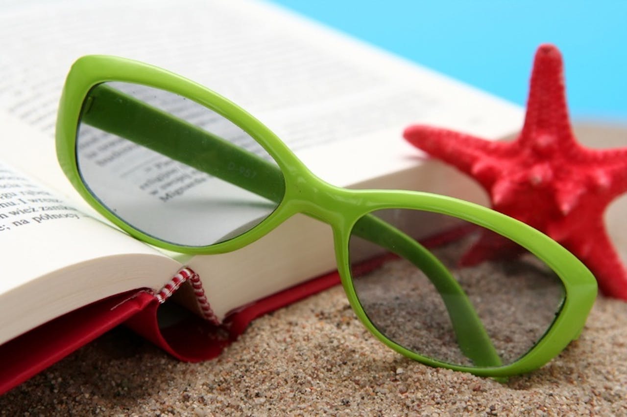 Een groene bril, een open boek en een rode zeester op het zand.