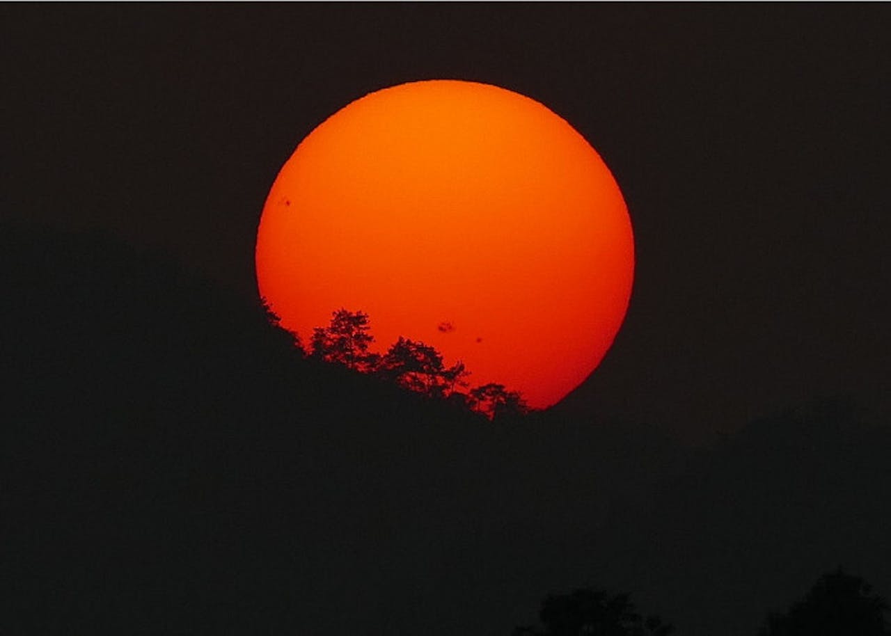 Een oranje zon voor een klein gedeelte achter een berg.