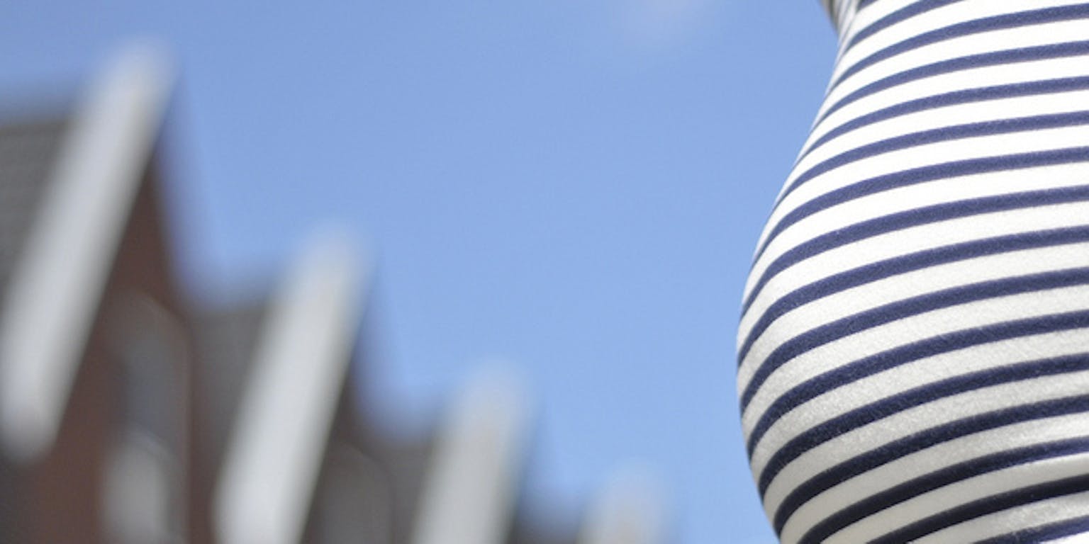 Een zwangere vrouw in een blauw-wit gestreepte jurk die voor een huis staat.