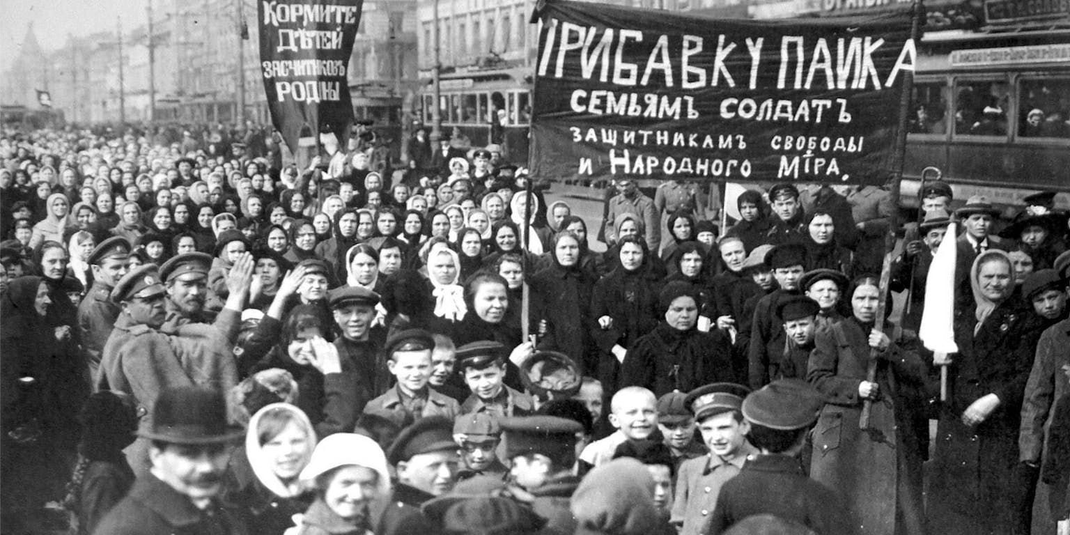 Een zwart-witfoto van de Putilov-arbeiders op de eerste dag van de februari-revolutie. Een menigte met spandoeken staat op straat en kijkt naar de camera.