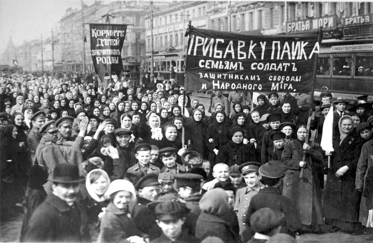 Een zwart-witfoto van de Putilov-arbeiders op de eerste dag van de februari-revolutie. Een menigte met spandoeken staat op straat en kijkt naar de camera.